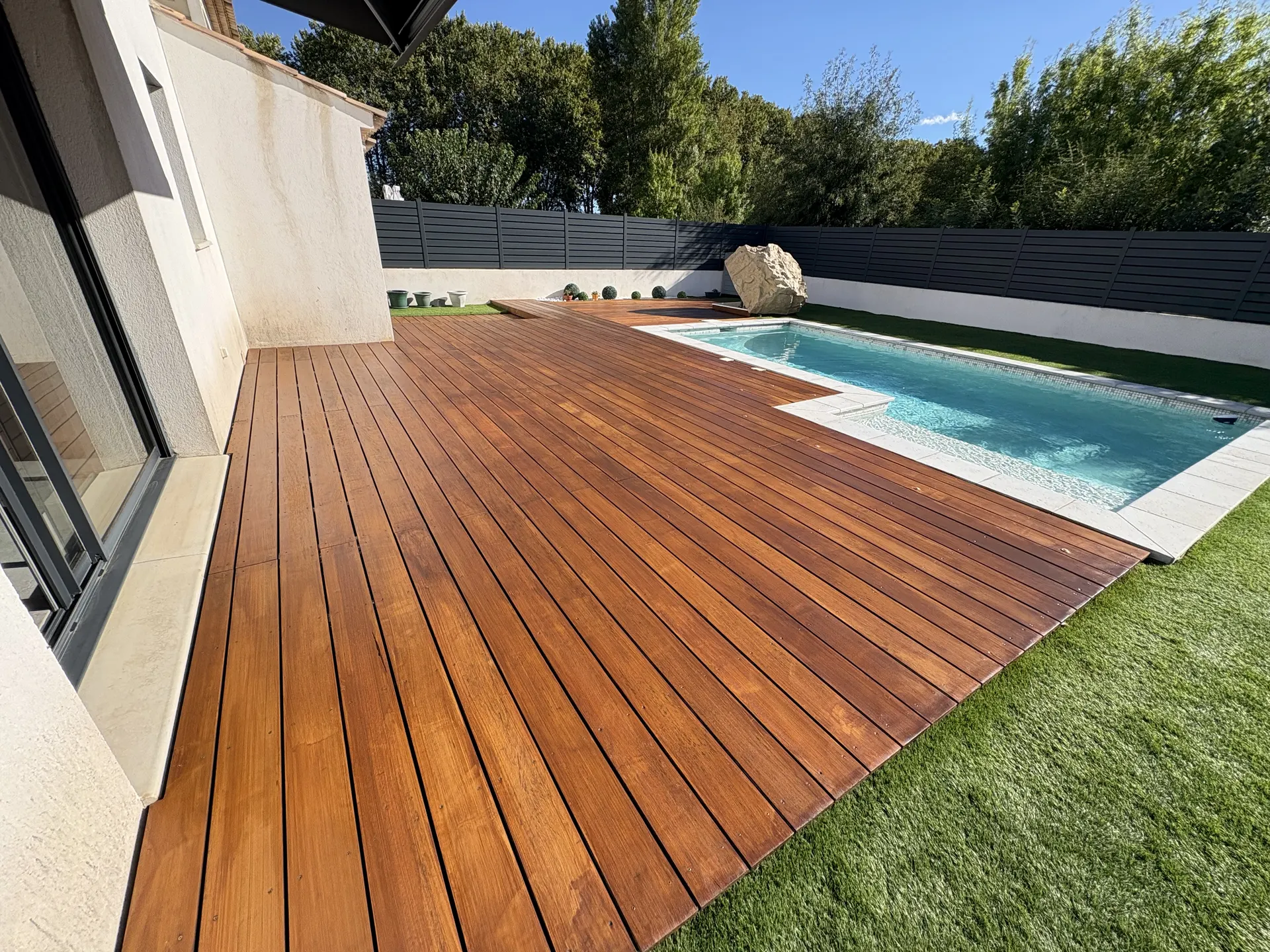 Terrasse en bois autour d'une piscine, bordée de gazon, après rénovation